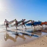 A line of surfers on the beach running towards the water