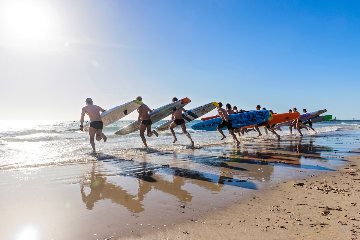 A line of surfers on the beach running towards the water