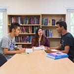 three students sitting around a desk and studying