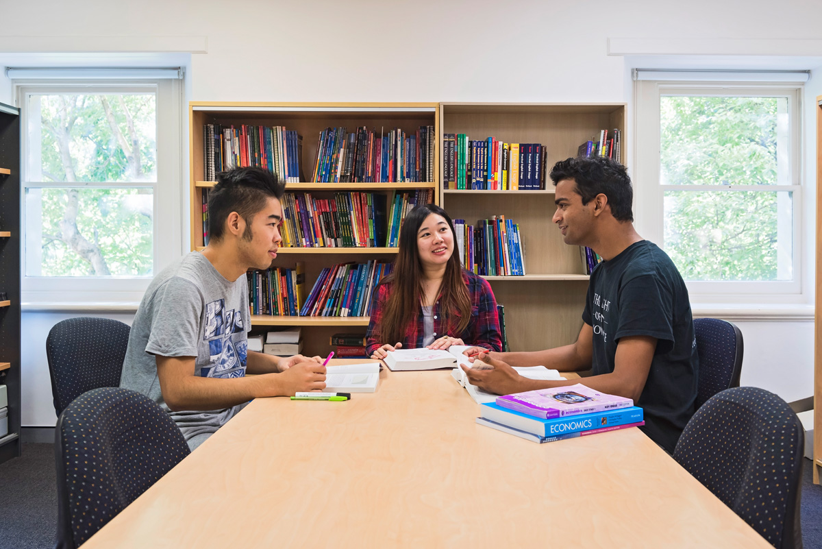 three students sitting around a desk and studying